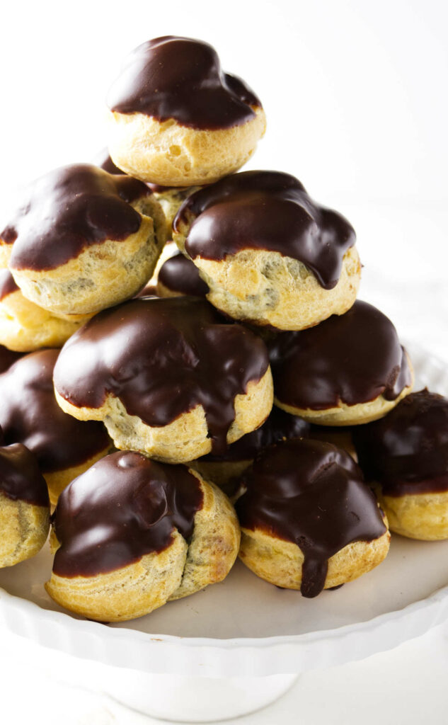 A stack of mini cream puffs (profiteroles) on a cake plate.