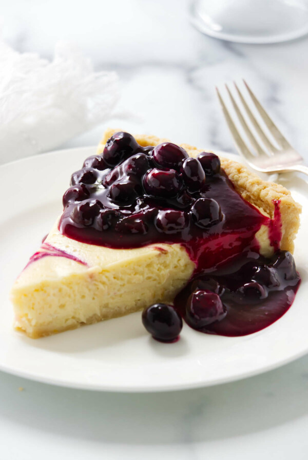 A slice of a lemon blueberry tart with blueberry sauce on top.