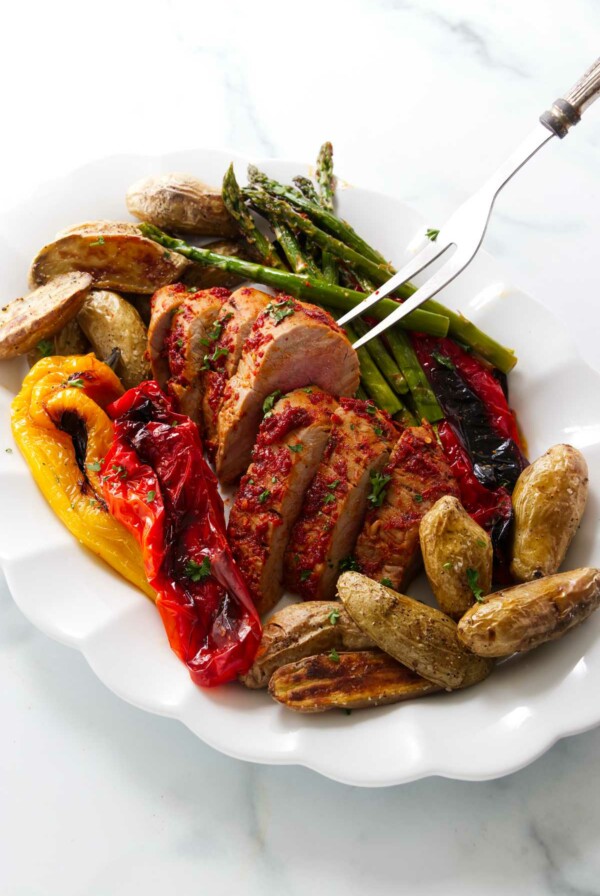 A pork tenderloin and vegetables on a serving platter.