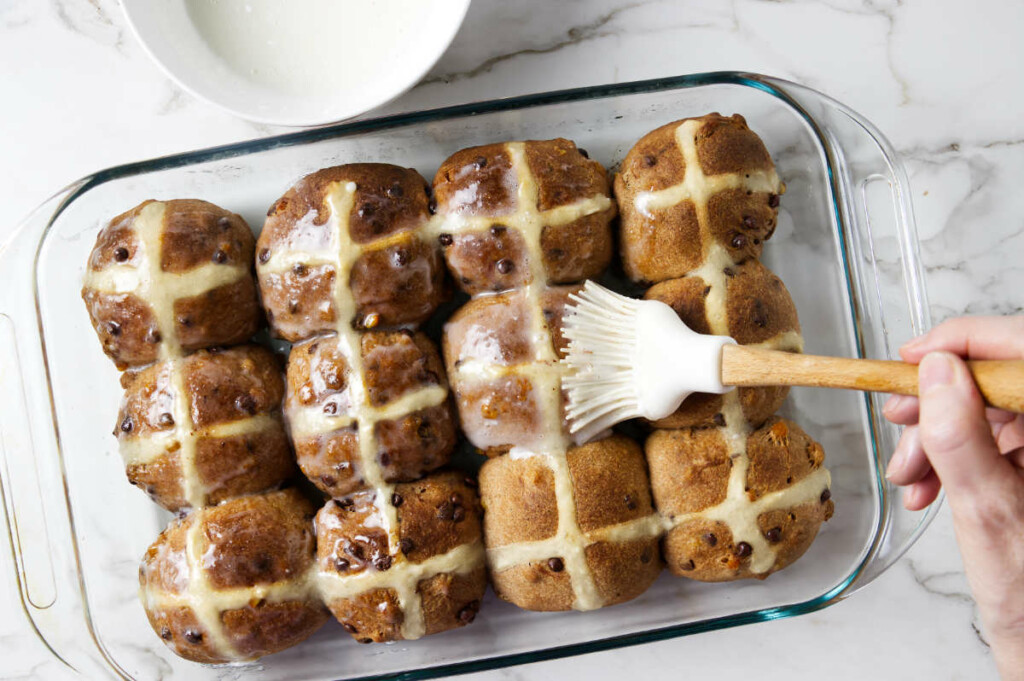 Brushing a glaze over warm hot cross buns made with whole wheat.