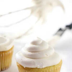 Close-up of a vanilla cupcake with swirled white frosting, blurred background.